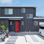 黒い外壁に赤い玄関ドアを合わせた2階建て住宅の外観
