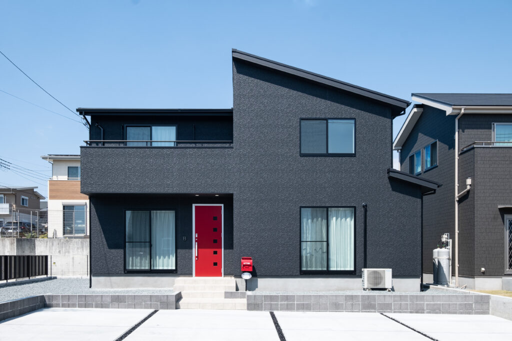 片流れ屋根と黒い外壁、赤い玄関ドアを組み合わせた2階建て住宅