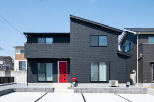 片流れ屋根と黒い外壁、赤い玄関ドアを組み合わせた2階建て住宅